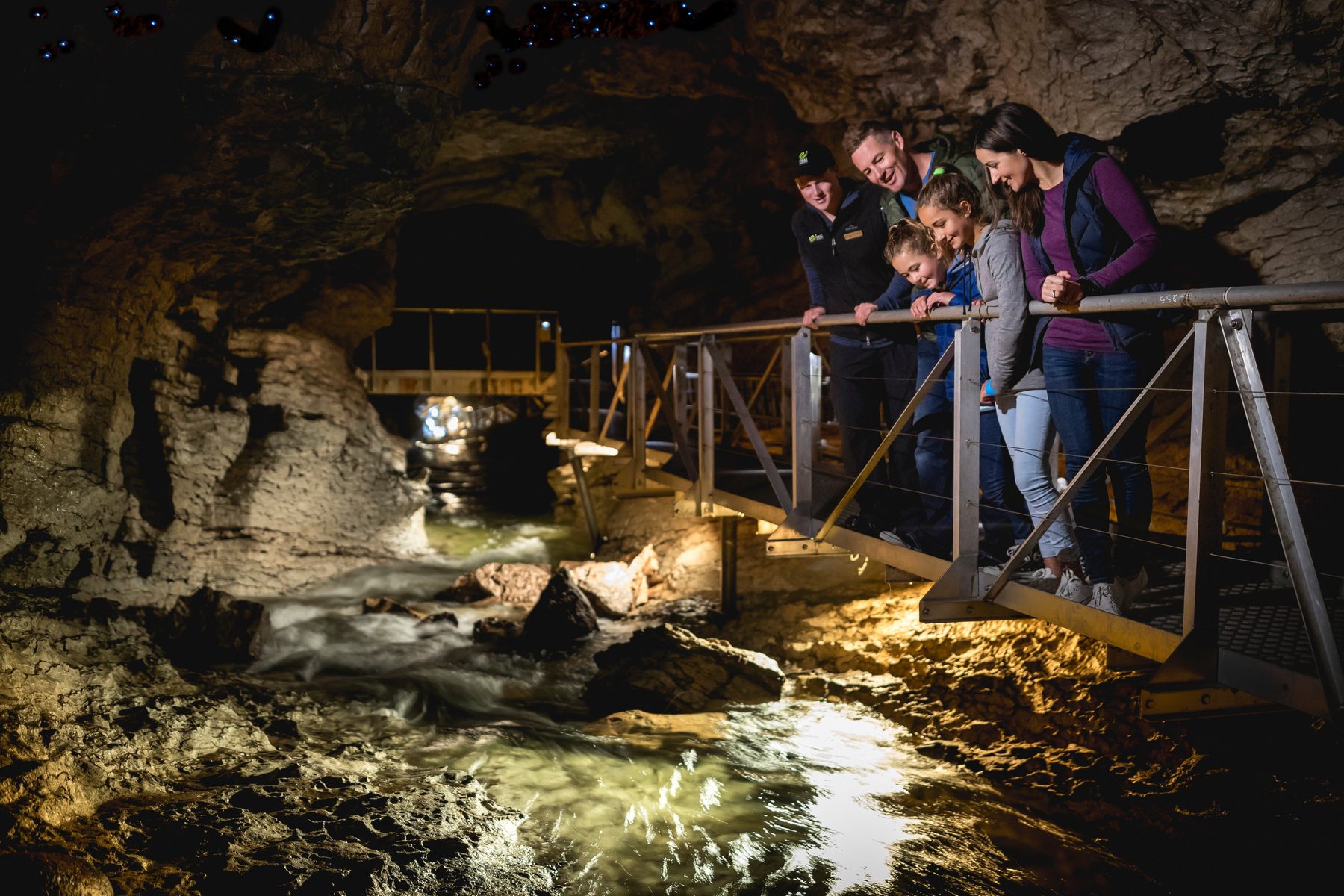 Guide and family watching the underground river from a cave walkway